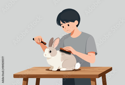 A person brushes a fluffy white and grey rabbit on a wooden table. The person smiles. Grey background