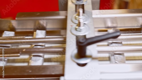 A close-up view of aluminum foil-wrapped chocolate bars moving rapidly along a stainless steel industrial conveyor track in a food factory, ready for final packaging.