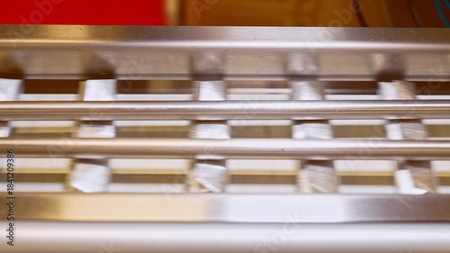A close-up view of aluminum foil-wrapped chocolate bars moving rapidly along a stainless steel industrial conveyor track in a food factory, ready for final packaging.