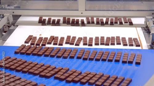 A close-up shot of chocolate bars moving in neat rows along a bright blue conveyor belt in a food production facility.