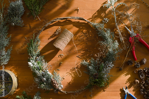A winter wreath being made of cypresses, fern, silver ragwort, and cones from various conifers