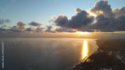 Aerial view of a golden sunset over the calm waters of Lake Issyk-Kul with dramatic clouds and sun reflection on the surface near the coastline