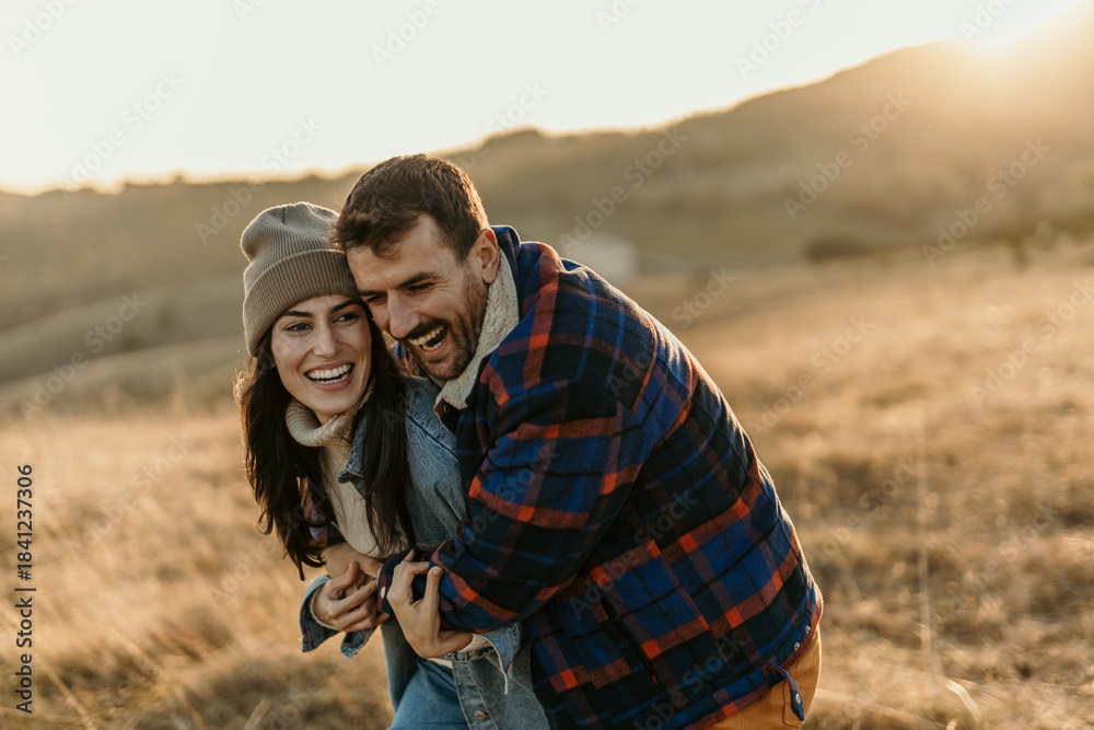 Fototapeta premium Cheerful young couple embracing laughing outdoors during sunset