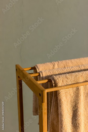 Soft, fluffy beige towels hang on a natural wood rack in a calm, warmly lit bathroom. A cozy, spa-like atmosphere ideal for home interior and lifestyle imagery.