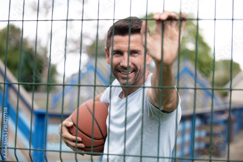 male basketball player leaning on fence holding ball outdoors