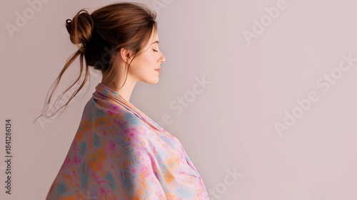 A pregnant woman in a soft pastel shawl gently holding her belly, smiling warmly in bright natural light against a clean minimal background.