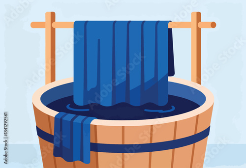 Blue fabric drying on wooden rack above wooden tub filled with dark liquid