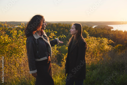 Women talking with each other standing on hill at sunset