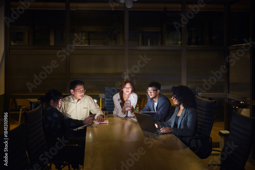 Female business professionals using wireless technologies while sitting in office meeting with male colleagues at night
