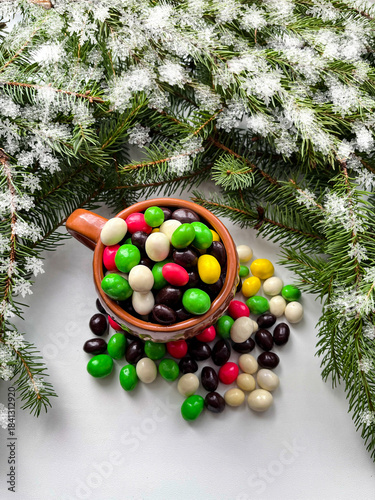 Computer illustration. Background for a holiday card. Fir branches, a cup with multicolored dragees and a frame of graphic snowflakes.