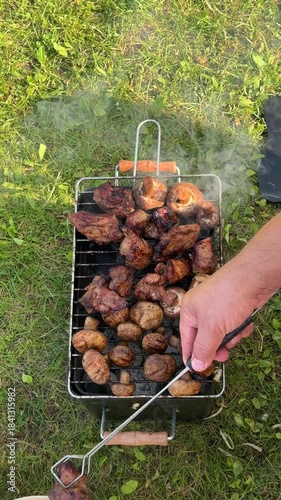 Grilling delicious marinated meat and mushrooms on a portable barbecue, showcasing the cooking process with smoke rising, camera pans and zooms in for detail