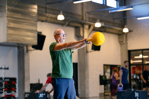 Active mature woman doing strength exercise with kettlebell in gym