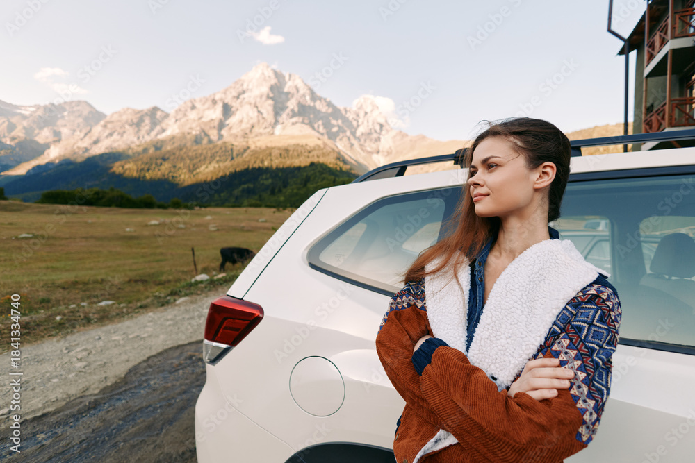 Naklejka premium Woman and car parked in countryside by mountains for travel and roadtrip, standing in sweater jacket with folded arms, scenic landscape, outdoor adventure and calm moment.