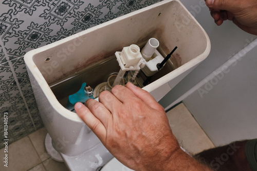 Plumber repairing or replacing the fill valve of a toilet flush tank.