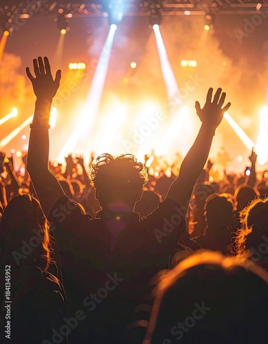 Audience member with raised hands enjoying a bright concert under stage lights.