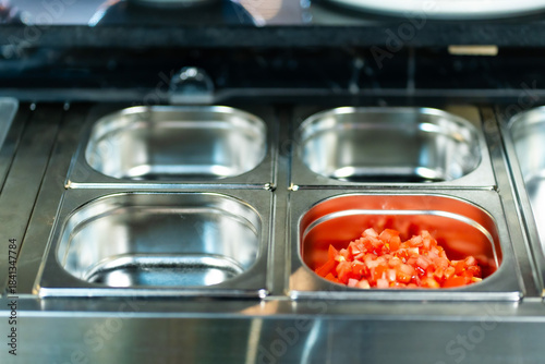 Metal containers filled with various sliced vegetables and ingredients in a professional kitchen setting