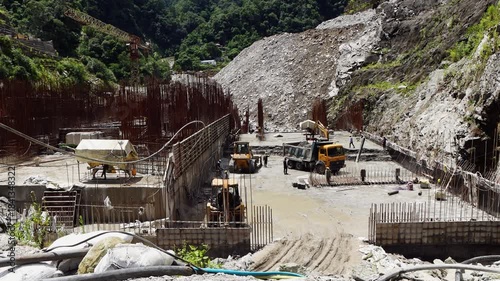 Civil engineering and industrial construction in Nepal Himalayas showing the process of building a hydropower dam with hydraulic excavators and dump trucks moving earth and stone.