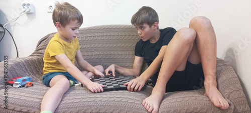 Εκτύπωση καμβά Two boys are playing chess on a sofa in their home.