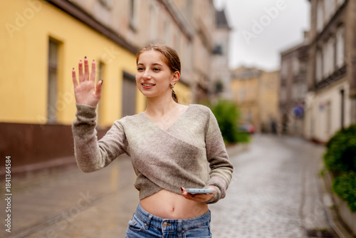 Young Woman Walking In Historic City Center Waves To Someone