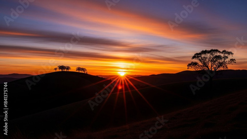Dramatic sunset over rolling hills with silhouetted trees