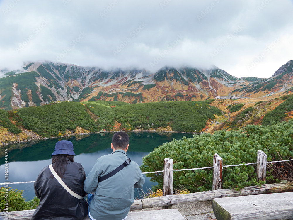 Naklejka premium 秋の観光名所立山黒部アルペンルートの室堂山頂のみくりが池で休憩するシニア男女観光客の姿と山の風景