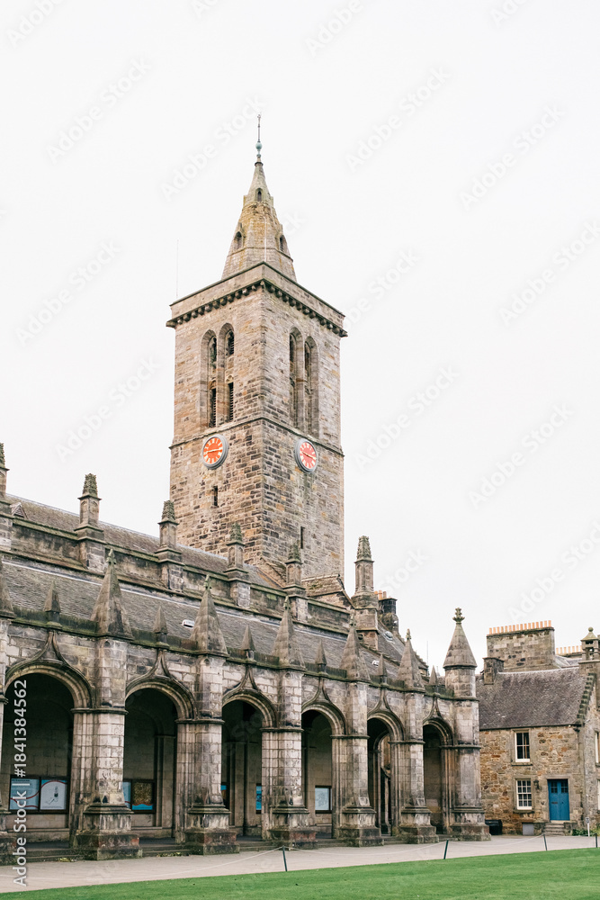 Obraz premium Old stone clock tower with arched walkway and courtyard, historic architecture under cloudy sky