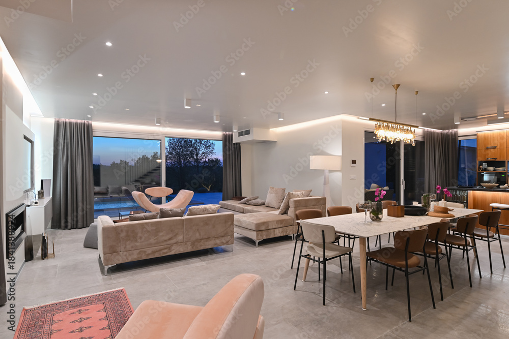 Obraz premium Modern luxury living room interior at sunset. Open-plan space featuring beige sofas, marble dining table, large glass windows with sun flare, and view of a patio. Stylish contemporary home design