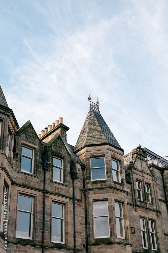 Fototapeta premium Detailed view of old stone building with pointed turret, chimneys, and windows beneath a blue sky 