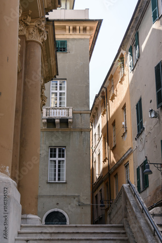 Vista de ángulo bajo de edificios históricos altos con fachadas coloridas y persianas en una calle estrecha europea bajo la luz del sol. Savona, Italia.