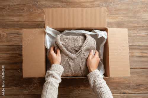 Returning unwanted gifts can be thoughtful process as hands carefully place cozy beige sweater into cardboard box on wooden table for shipping or exchange