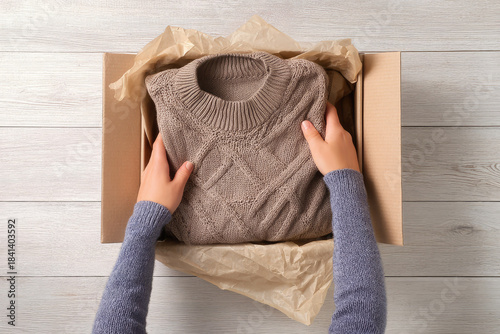 Returning unwanted gifts can be emotional as hands carefully place knitted sweater into cardboard box for return shipping on wooden table background