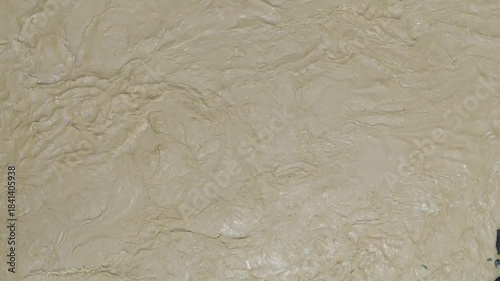 Aerial top down view of muddy brown river water flowing rapidly with swirls and turbulence during the monsoon season creating a natural abstract texture background