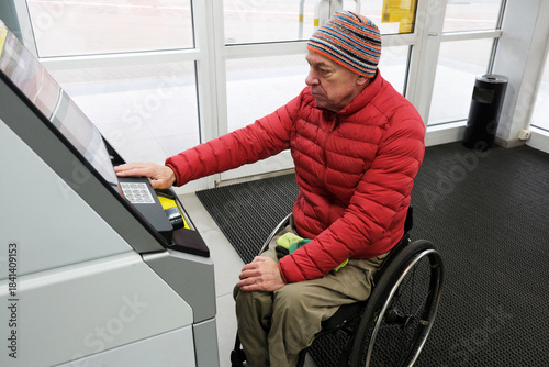 A man in a wheelchair prepares to enter his PIN at an ATM.