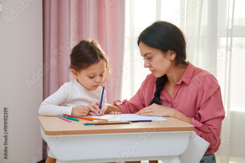 Mother and cute little daughter drawing with colored pencils, engaging in creative home learning