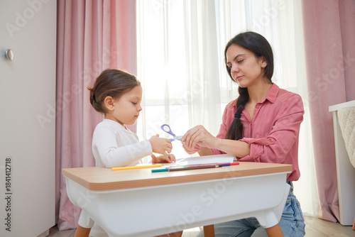 Mother and daughter cutting designs from paper with scissors for an art project