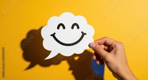 Hand Holding Happy Face Speech Bubble Cutout on Yellow Background Symbolizing Positive Communication