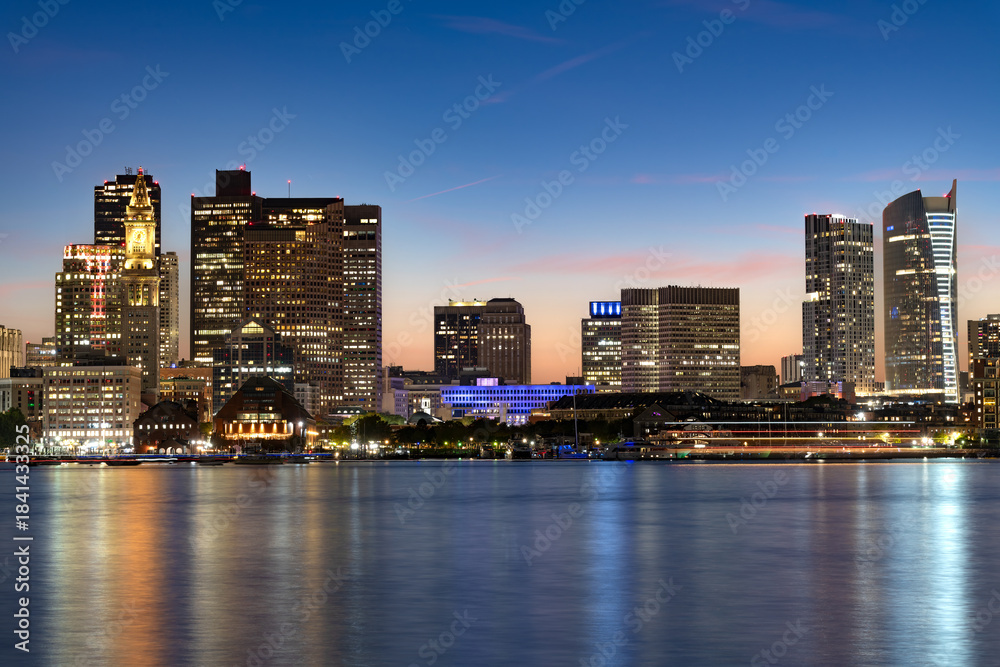 Obraz premium The vibrant lights of Downtown Boston reflecting on the water just after sunset, showcasing the urban beauty of the New England city.
