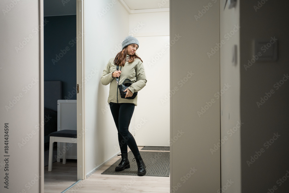 Fototapeta premium Woman leaving house. Checking outfit from mirror before exiting home door. Preparing to going to work in doorway. Going out from apartment. 