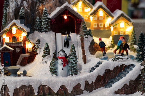 Fabulous New Year decorations. Glowing toy houses, snowman, decorative snow.