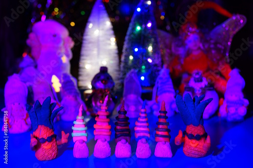 Figures of colorful gnomes and pineapples on the background of Christmas toys: fairies, snowman, angels.