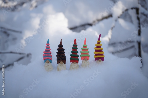 Colorful toy gnomes made of plasticine in the forest against a background of snow. Fabulous scenery.