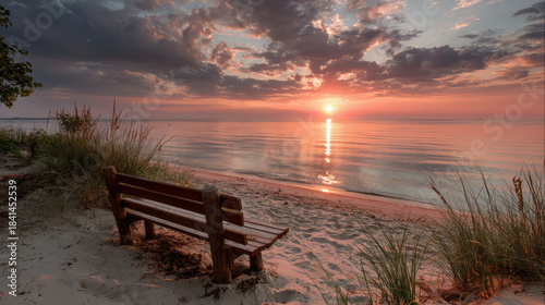 Peaceful empty wooden bench on calm sandy beach at sunset. Serene coast with beautiful sky and sunbeam reflecting on water