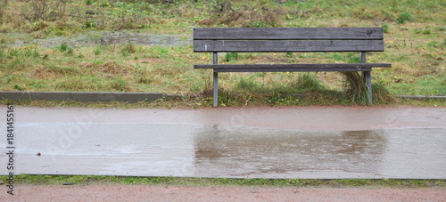 An old wooden park bench near a dirt path during the rain