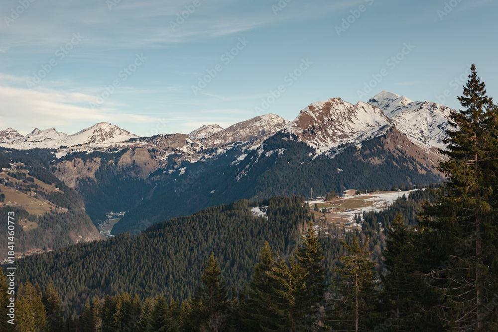 Fototapeta premium Snow-capped mountains and forested valleys near Les Gets, French Alps, under clear winter skies