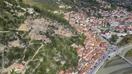 Aerial view of Berat showing hillside homes beneath the rocky slope leading to the castle and the Osum River crossing below.