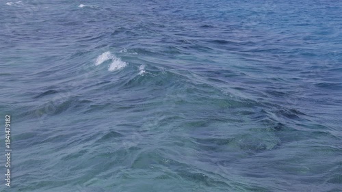 Gentle ocean waves undulate across the surface, showcasing varying shades of blue and turquoise. Slow motion.