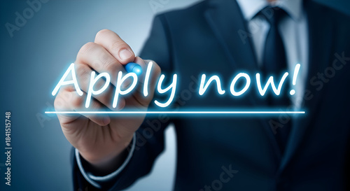 Businessman in a dark suit uses a glowing blue stylus to write the urgent call to action apply now across a digital interface symbolizing opportunity and immediate response