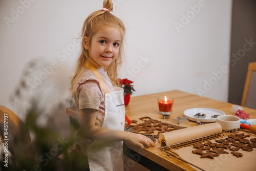 Child makes cookies in the kitchen with holiday decorations and candlelight in the afternoon
