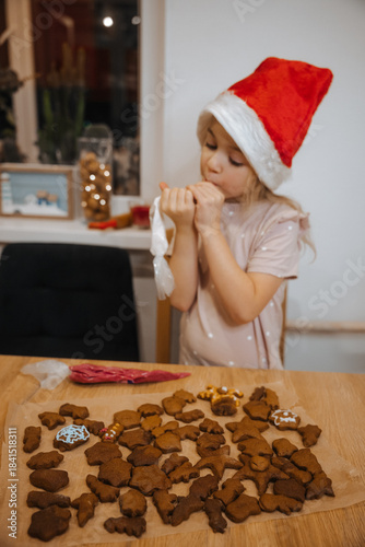 Child decorating cookies during Christmas holiday in home kitchen with festive hat