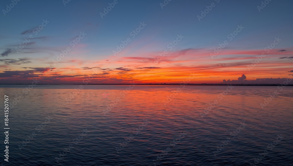 Obraz premium Vivid sunrise illuminating a broad river with reflected clouds and gentle water ripples, suitable for editorial header backgrounds